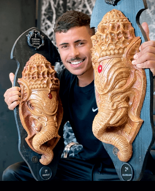 Lucas Nascimento holding two tattoo convention trophies, first place in portrait and second in realism
